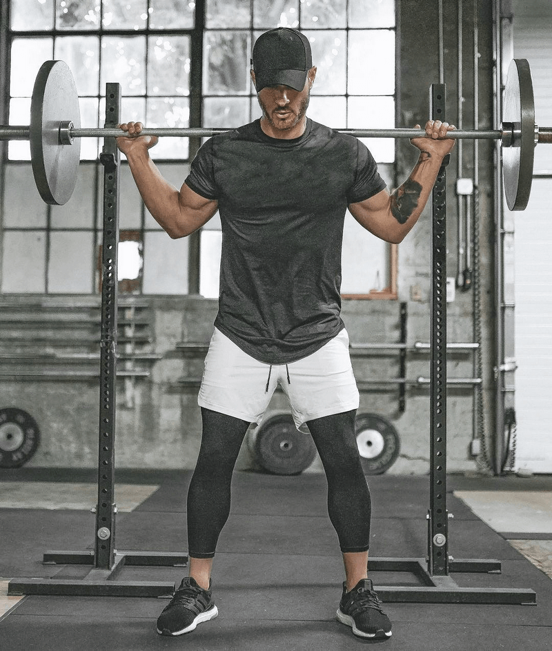 Man wearing a stylish black O-neck t-shirt and shorts, lifting weights in a gym.